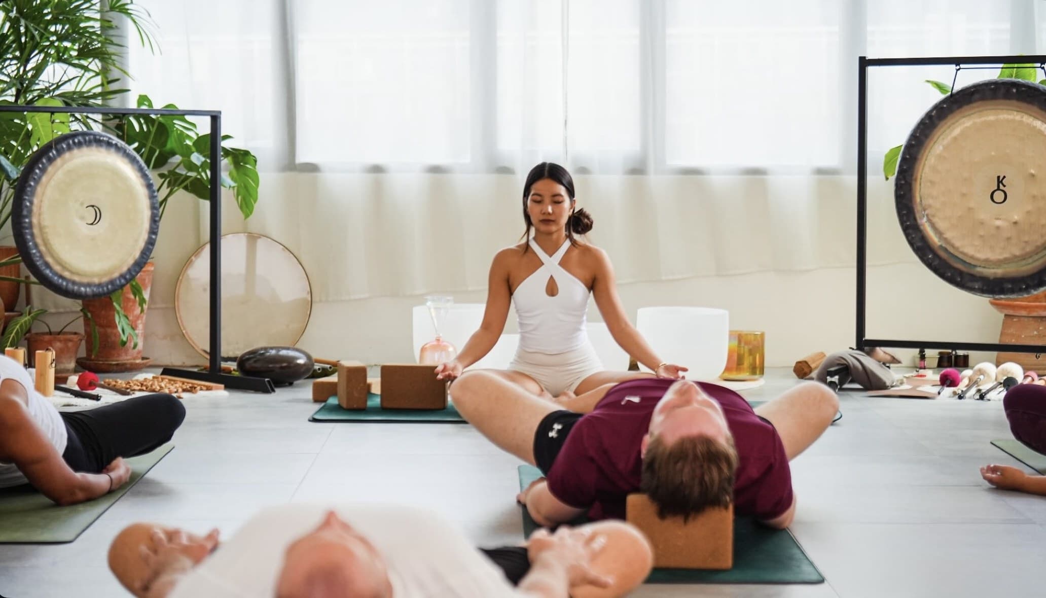 Yok seated between two gongs leading a sound bath in a softly lit Bangkok studio
