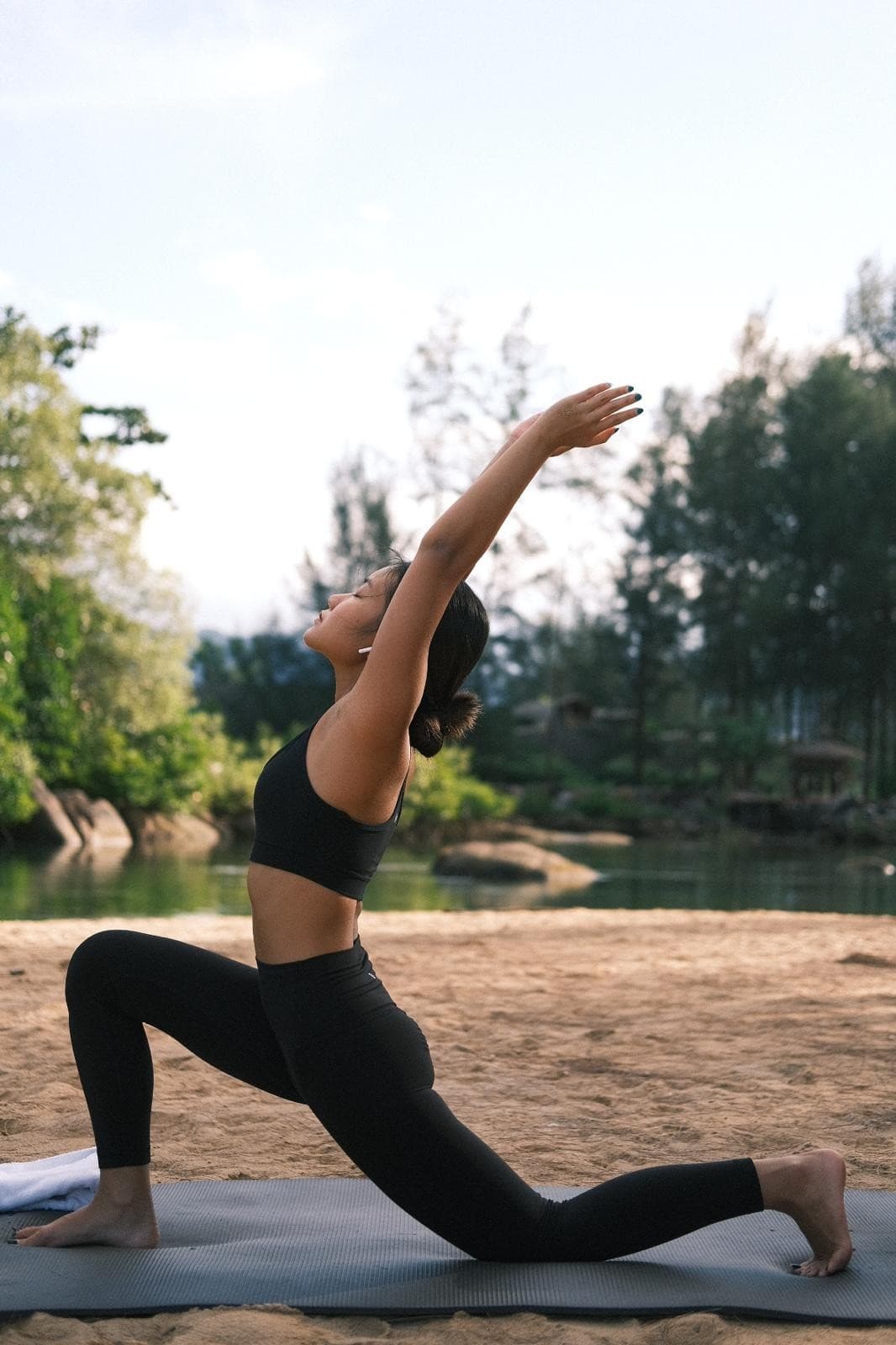 Yok in a low lunge with arms raised by a forest lake at sunrise